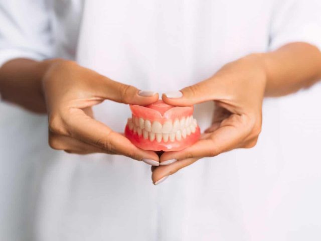 The dentist is holding dentures in his hands. Dental prosthesis in the hands of the doctor close-up. Front view of complete denture. Dentistry conceptual photo. Prosthetic dentistry. False teeth